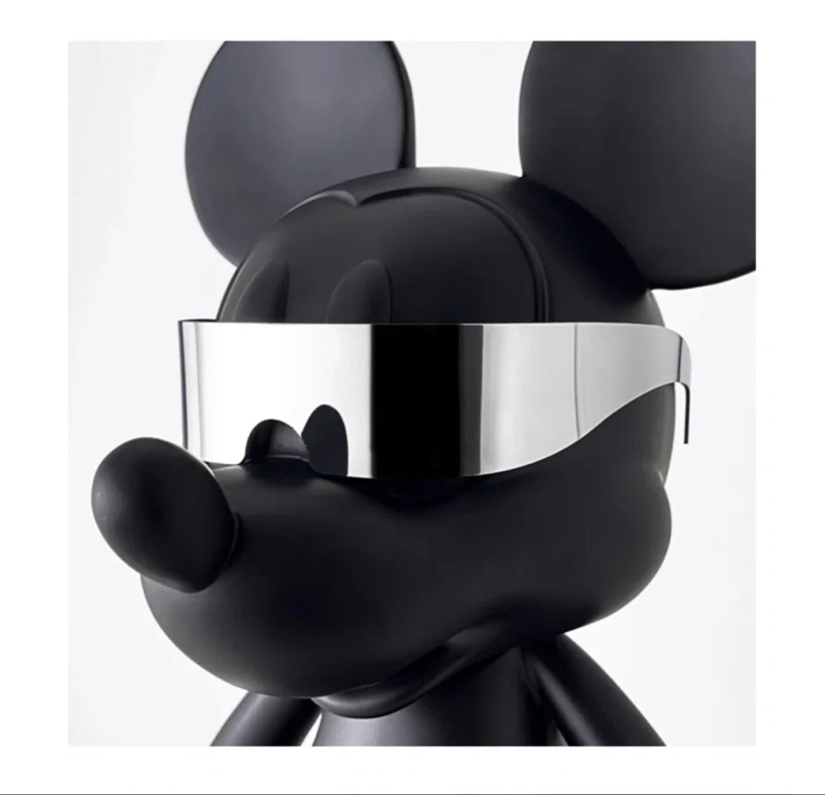 Närbild på huvudet av den svarta Mickey Mouse-figuren med släta linjer och reflekterande silvriga handskar i närheten.