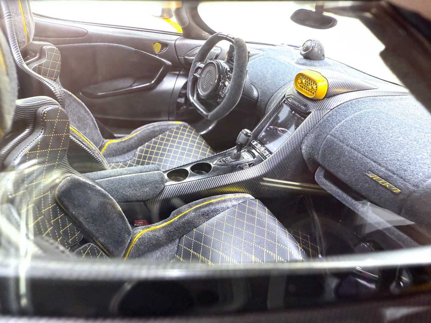Närbild av kupén i Koenigsegg Jesko Carbon Fury Edition med gul-accenterade racingsäten, kolfiberinstrumentpanel och ett högpresterande rattarrangemang.