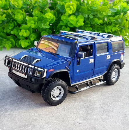 A 1:24 scale diecast metal model of a HUMMER H2 vehicle, primarily in green color, with the door open, displayed against a backdrop of lush greenery.