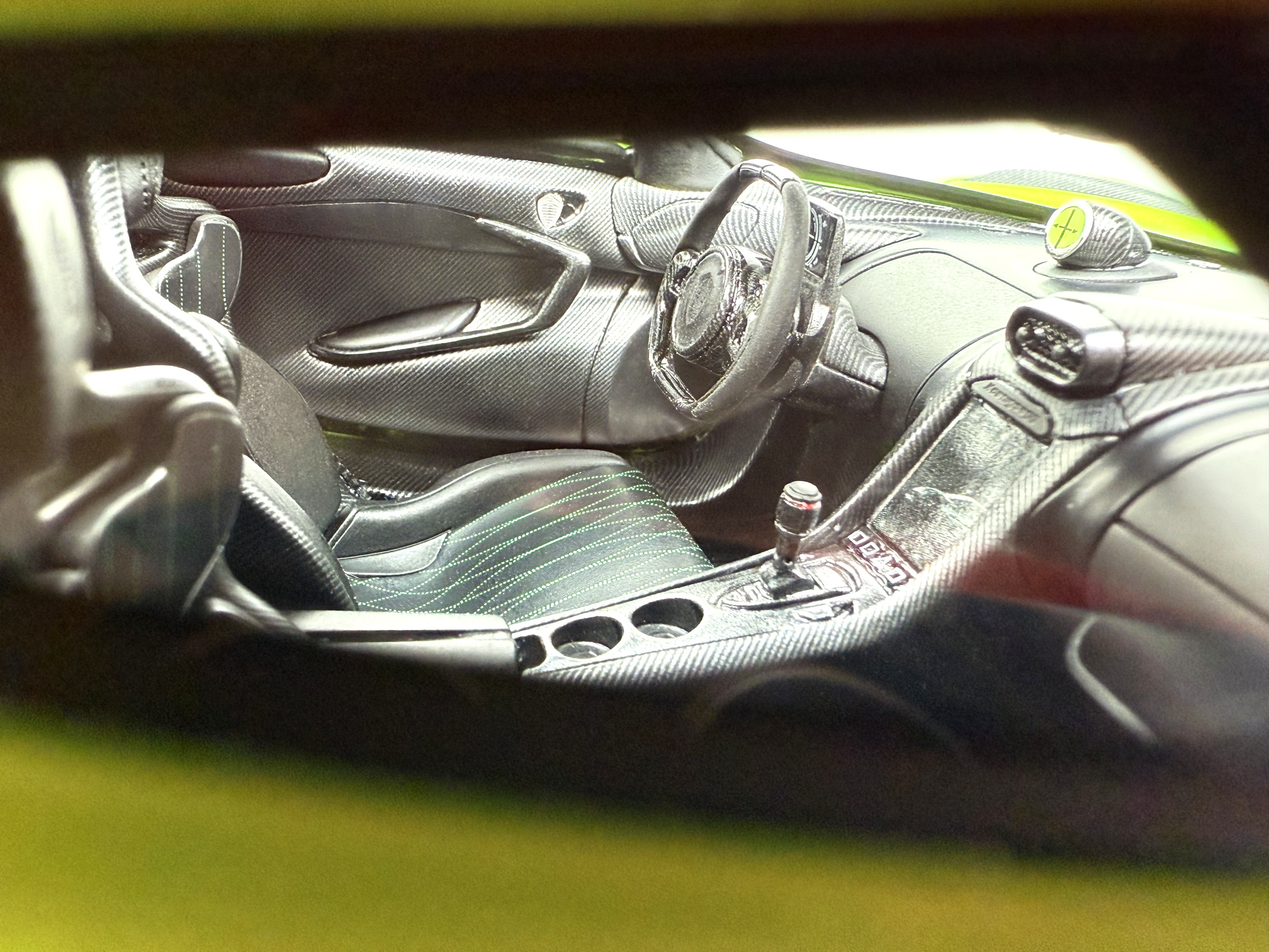 En detaljerad vy av interiören i Koenigsegg Jesko Absolut Venom Line Edition 1:18, som visar kolfiberdetaljer, lädersäten med grön söm och en slimmad ratt.