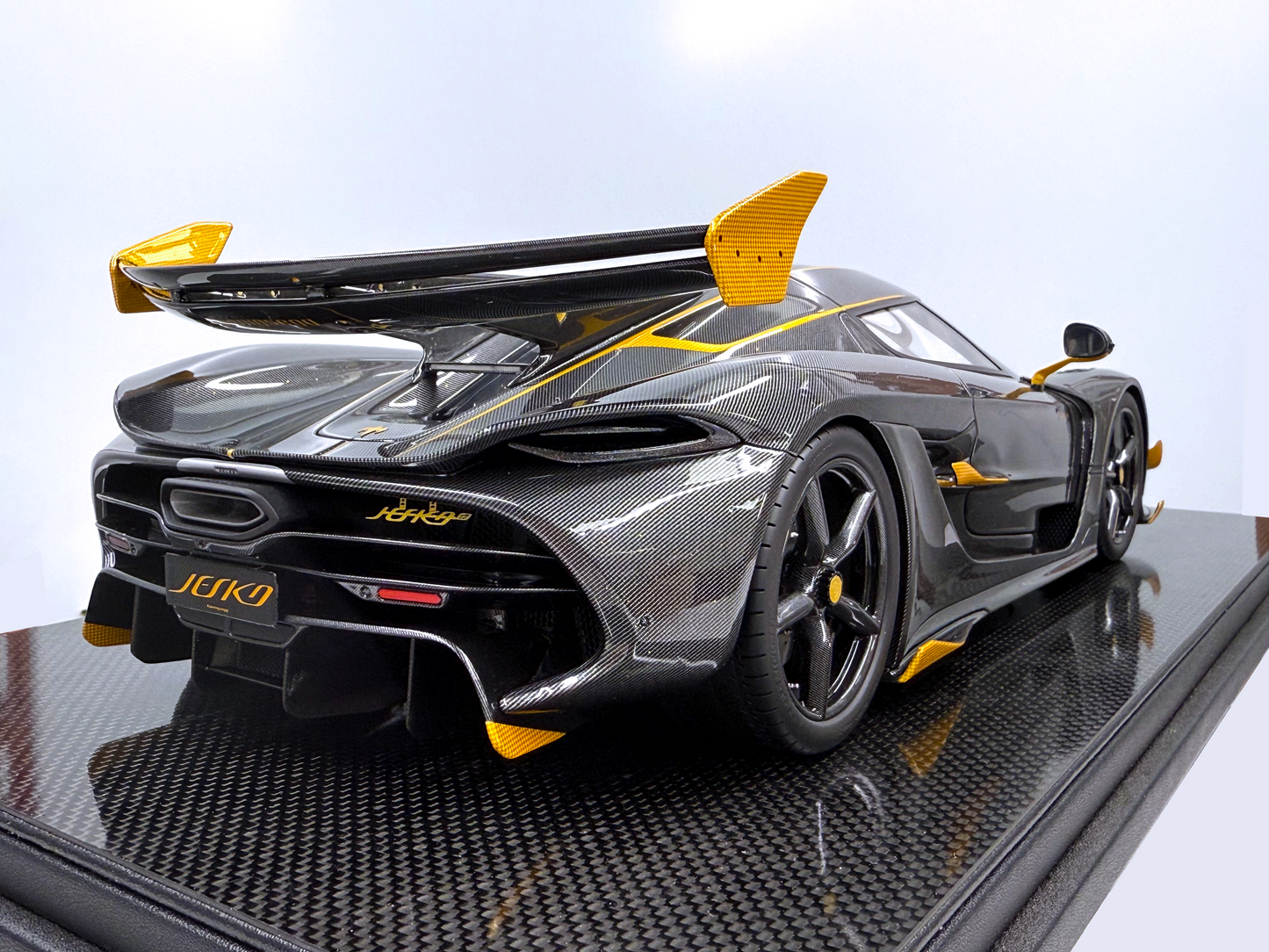 Bakifrån vy av Koenigsegg Jesko – Carbon Fury Edition i skala 1:8 som framhäver den aggressiva diffusorn, synligt kolfibermönster och kraftfulla gula detaljer längs bakvingen.
