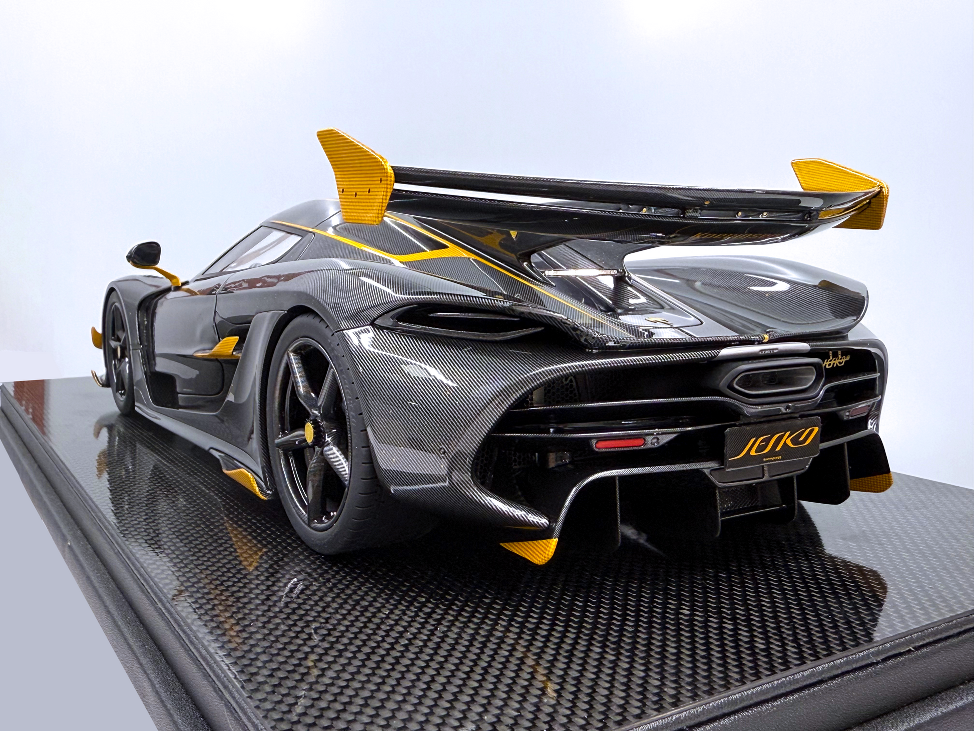 Bakifrån vy av Koenigsegg Jesko – Carbon Fury Edition i skala 1:8 som framhäver den aggressiva diffusorn, synligt kolfibermönster och kraftfulla gula detaljer längs bakvingen.