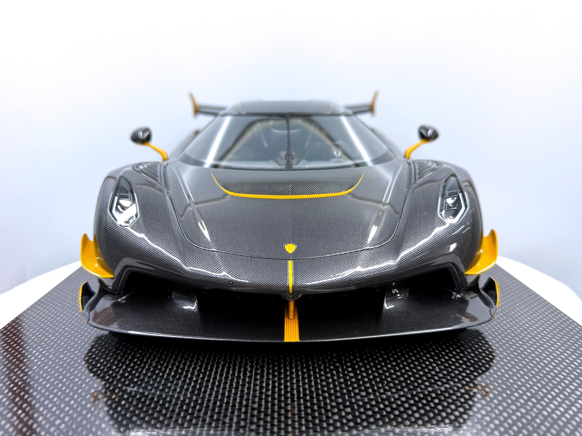 Från sidan framvy av Koenigsegg Jesko – Carbon Fury Edition i skala 1:8, med rå kolfiberkaross, gula accenter och aerodynamiska linjer.
